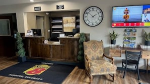 Un área de recepción con un escritorio de madera, un sillón estampado, un reloj de pared y un televisor mostrando una caricatura.