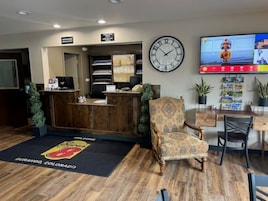 Un área de recepción con un escritorio de madera, un sillón estampado, un reloj de pared y un televisor mostrando una caricatura.