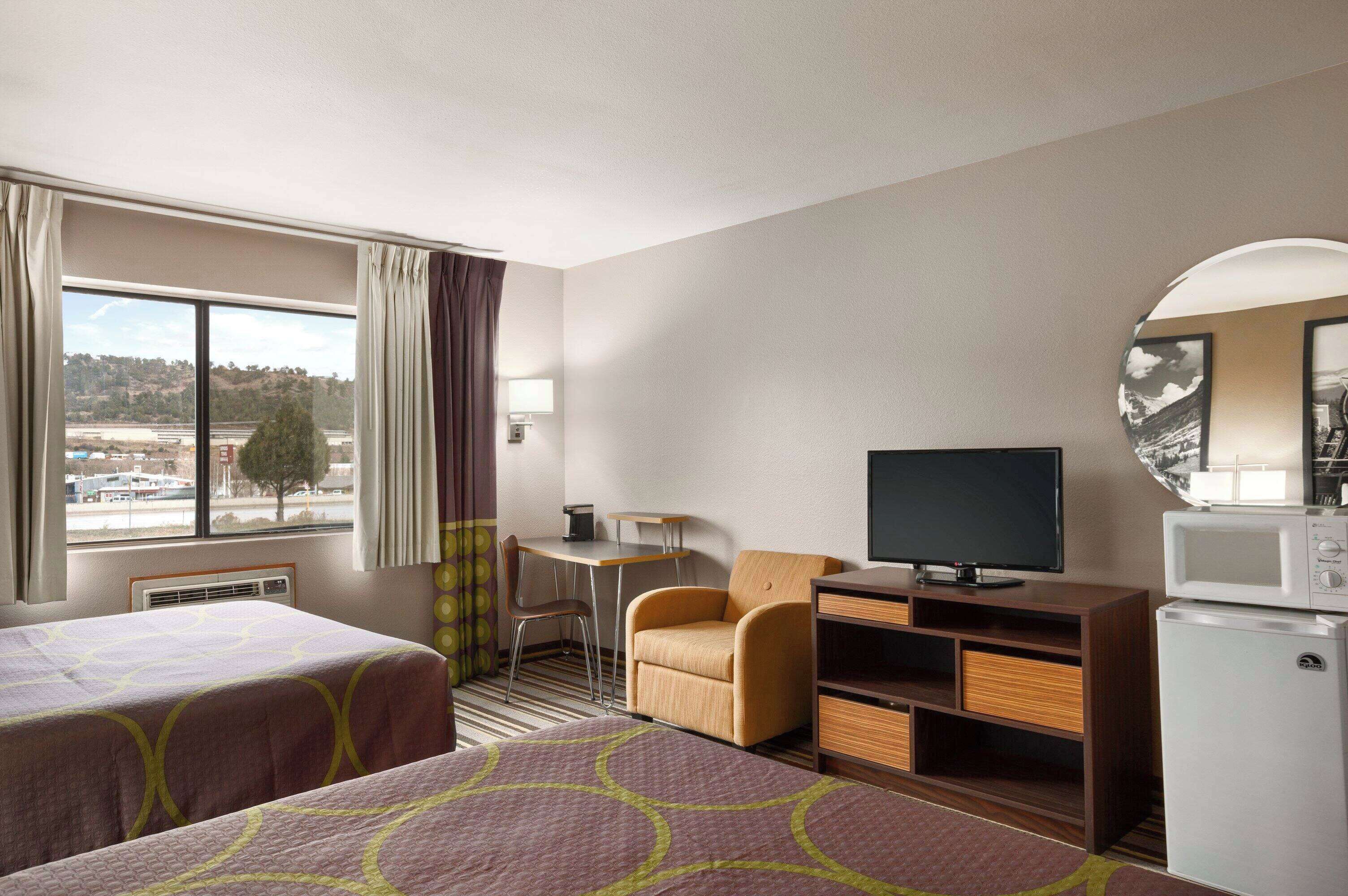 Ein Hotelzimmer mit zwei Betten, einem Schreibtisch, einem Sessel, einem Fernseher und einem Kühlschrank.