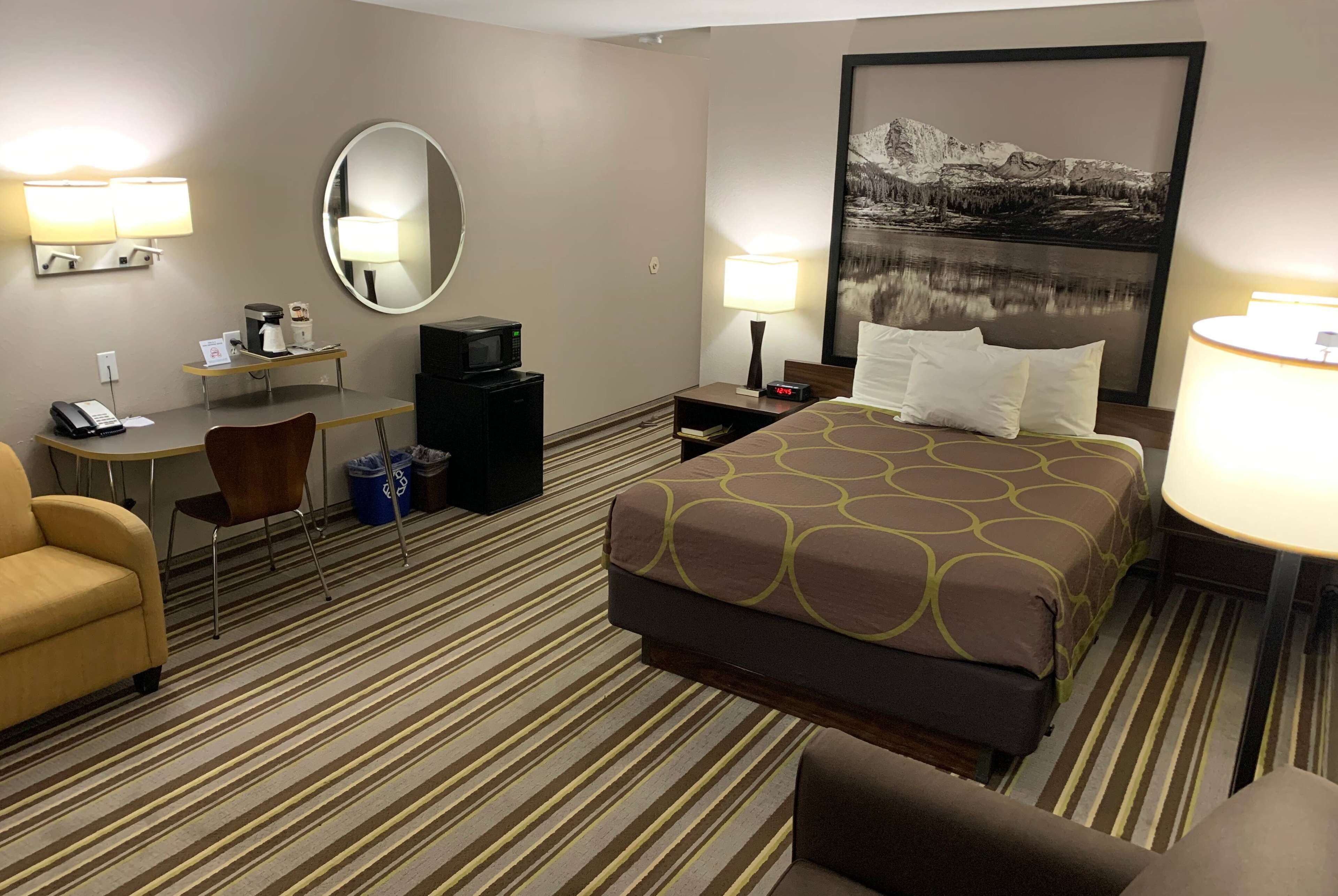 Une chambre d’hôtel avec un lit, un bureau, une chaise, un miroir, une lampe et un tableau au mur.