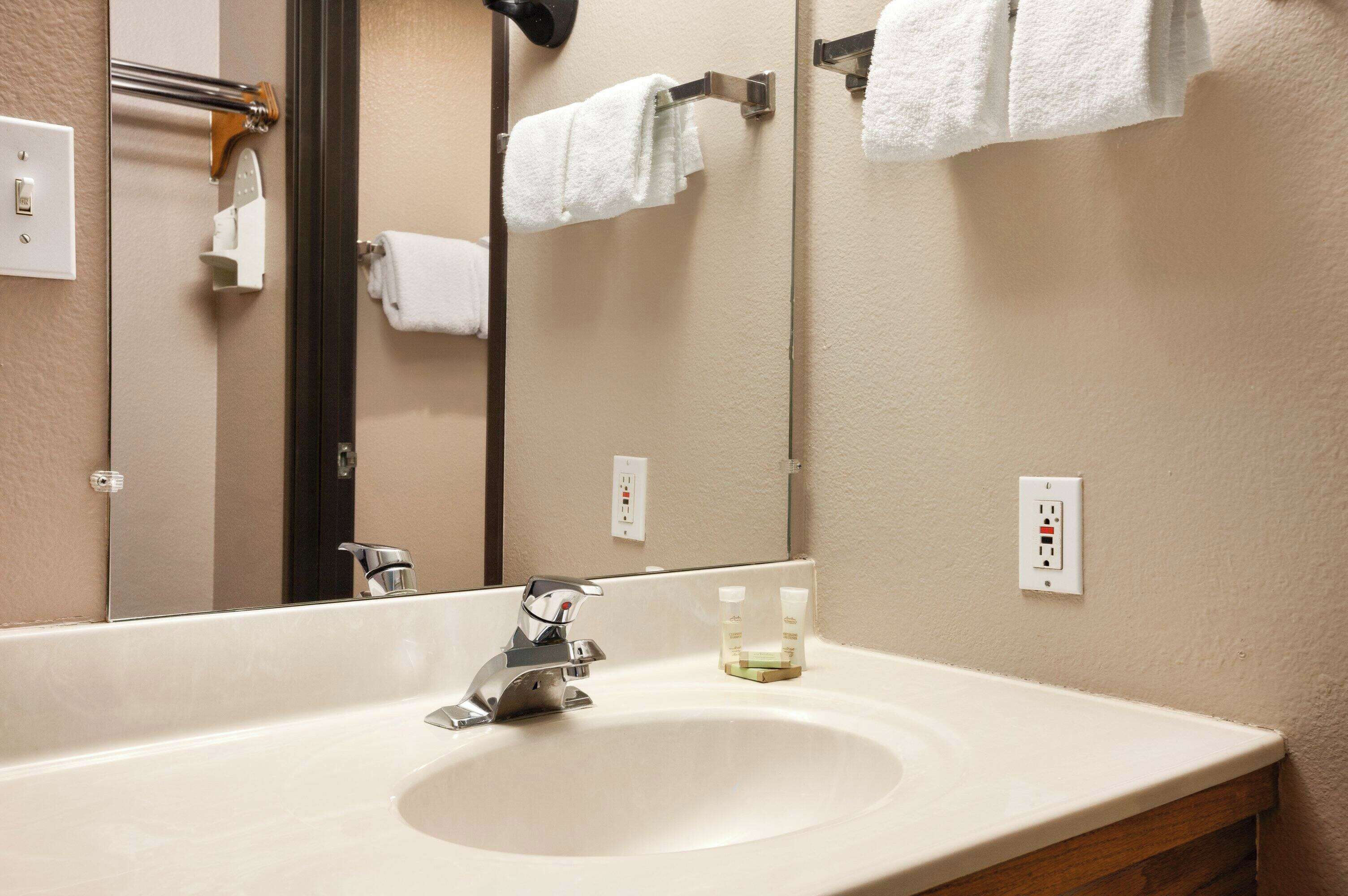 A bathroom with a large mirror, a sink, and a towel rack.
