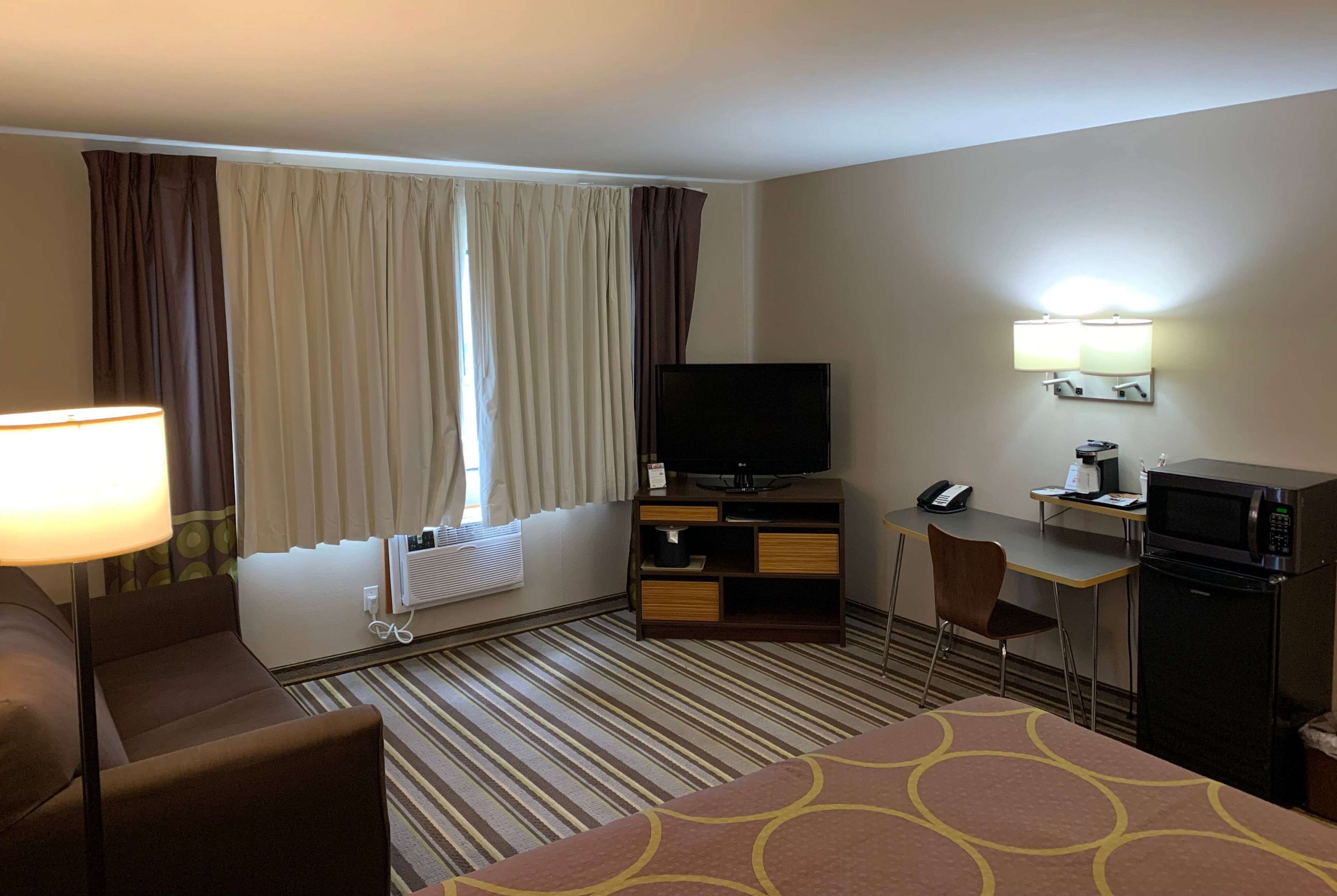 A hotel room with a bed, a desk, a television, a microwave, and a chair.