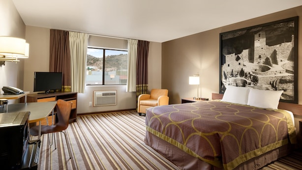 Habitación de hotel con cama, escritorio con silla, televisor y ventana grande.