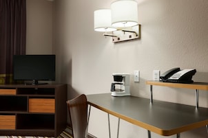 A hotel room with a TV, a coffee maker, a phone, and a wall-mounted lamp.