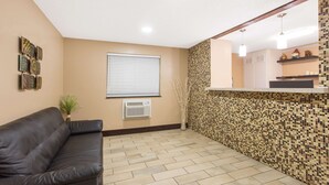 Ein Zimmer mit einer schwarzen Ledersofa, einem Fliesenboden, einer Wand-Klimaanlage, einem Fenster mit Jalousien und einer Wandverkleidung aus Mosaikfliesen.