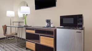Ein Hotelzimmer mit Schreibtisch, Stuhl, Mikrowelle und Flachbildfernseher.