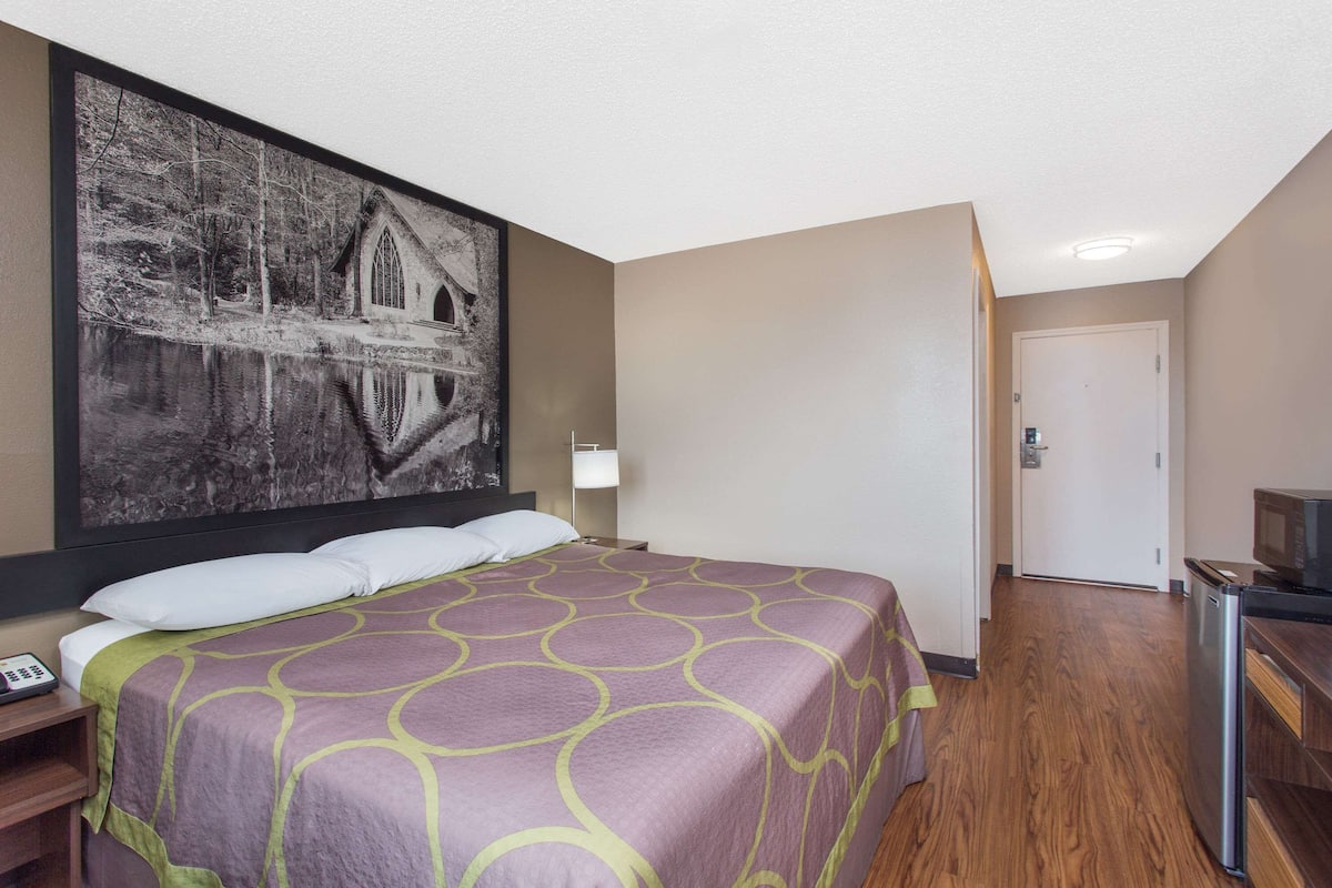Una habitación de hotel con una cama grande, televisión, escritorio y un cuadro en la pared.