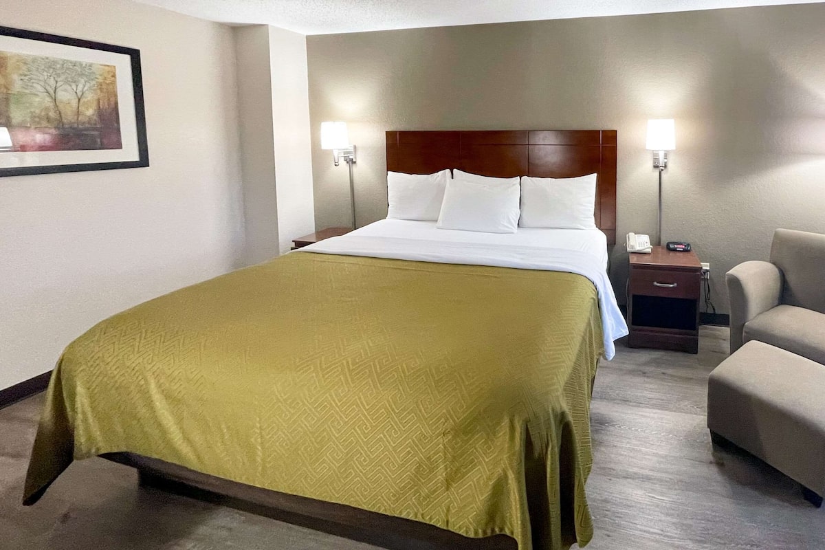 Habitación de hotel con una cama grande, dos mesitas de noche, una silla y un cuadro enmarcado en la pared.
