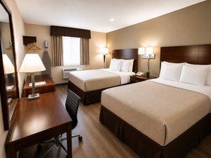 Habitación de hotel con dos camas, un escritorio, una silla, una lámpara y un espejo.