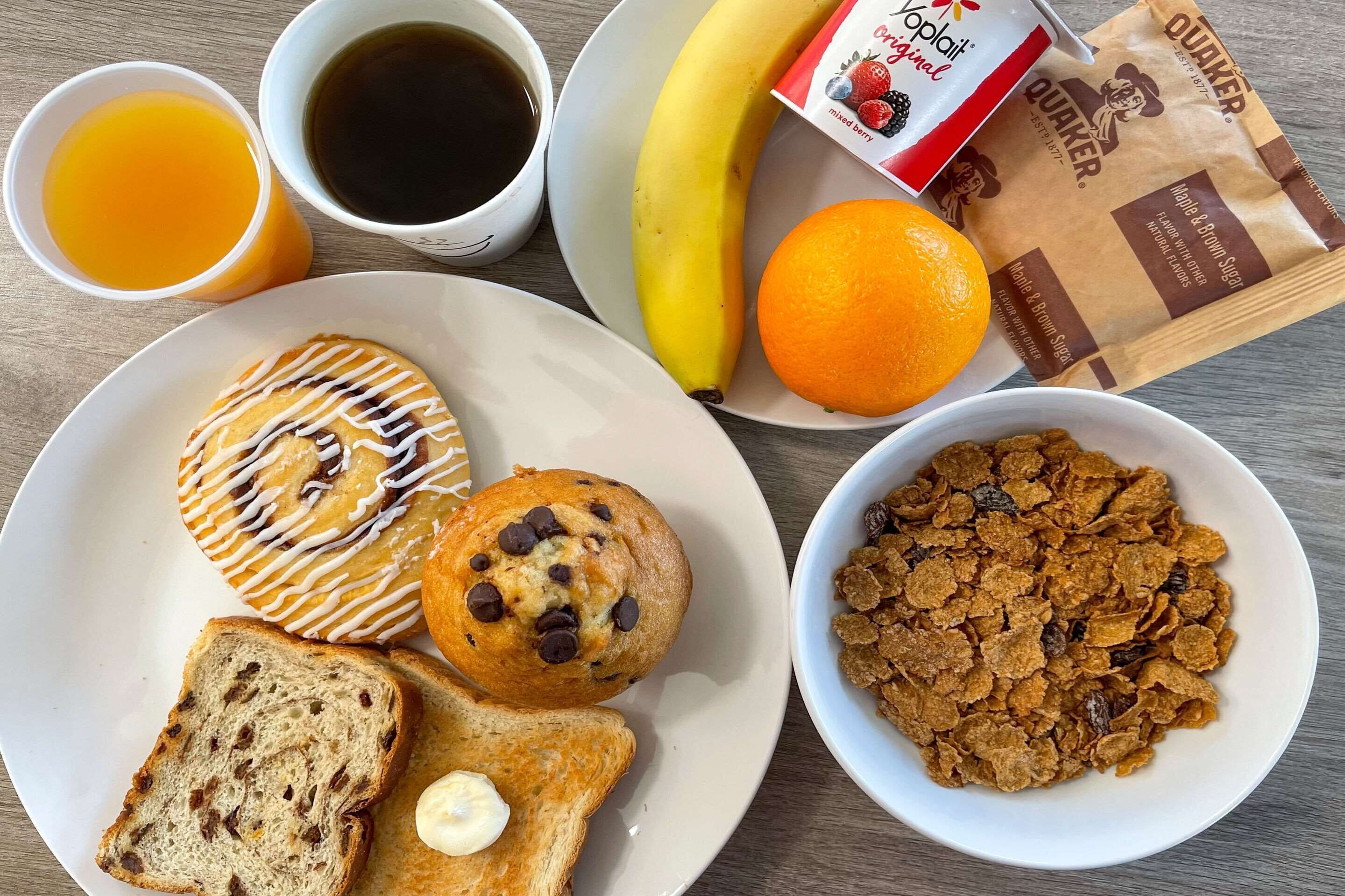 Un plato de desayuno con muffins, tostadas y cereales, junto con un plátano, naranja, café y jugo.