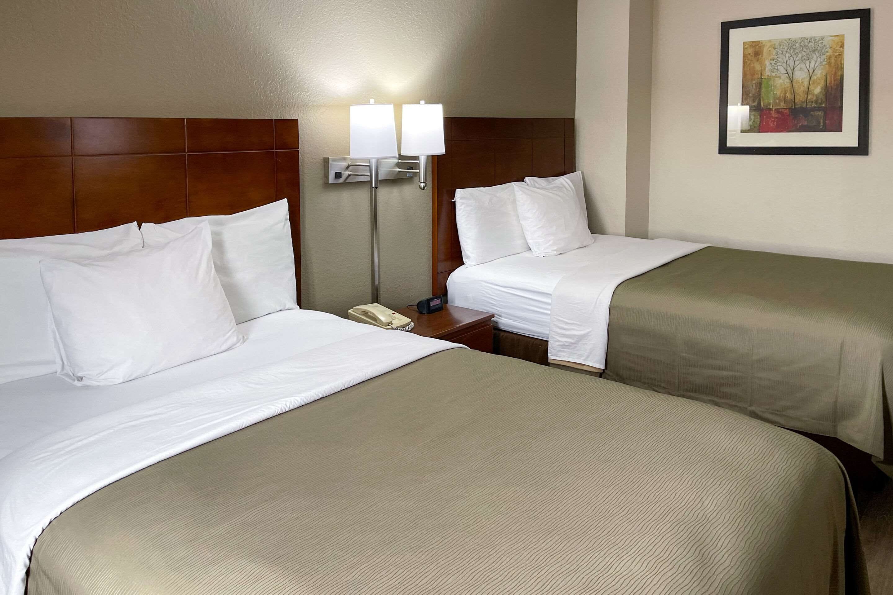 Habitación de hotel con dos camas, una mesita de noche con teléfono y una lámpara de pared.