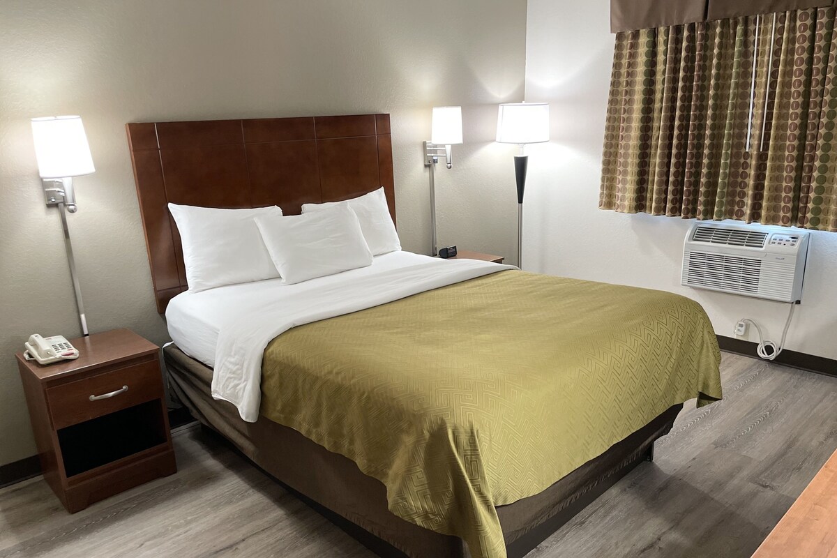Habitación de hotel con cama, dos lámparas de noche, un teléfono, mesita de noche y unidad de aire acondicionado.