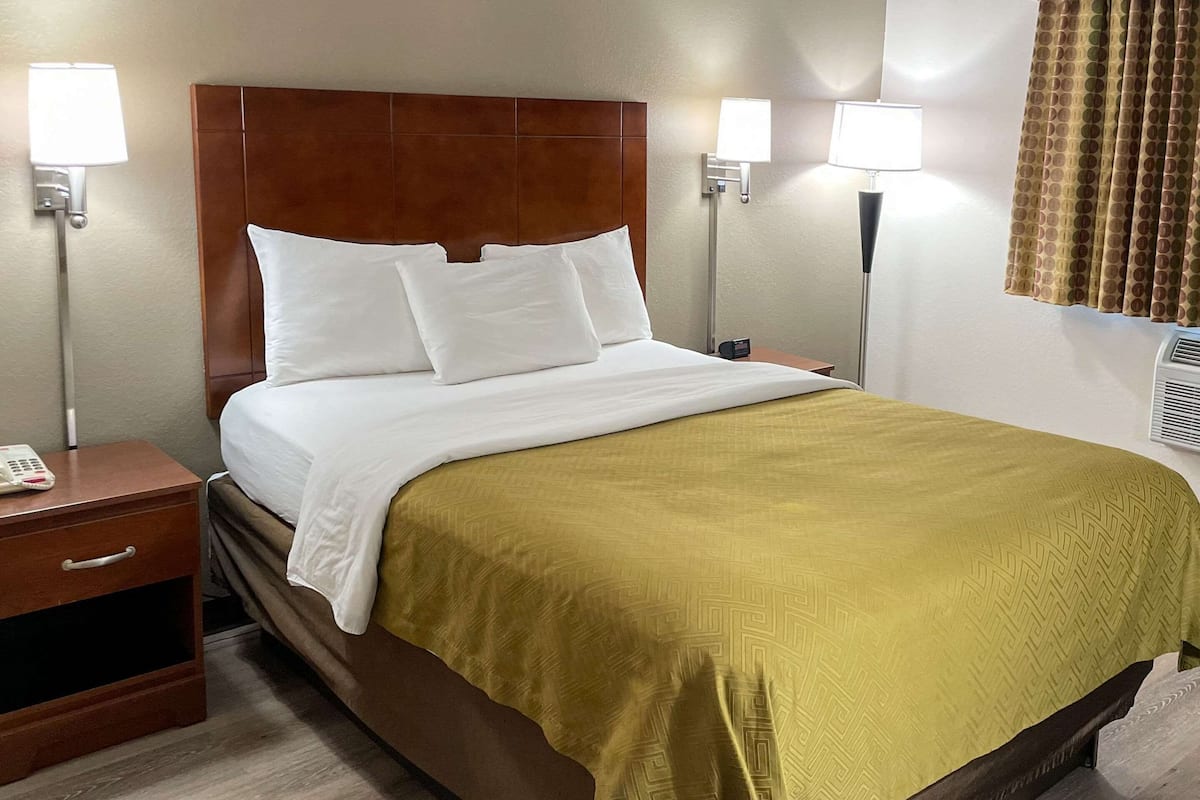 Una habitación de hotel con cama, mesitas de noche, lámparas y una ventana con cortinas.