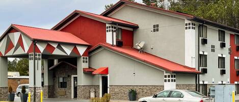 A multi-story hotel with a red and white facade, a covered entrance, and a car parked in front.