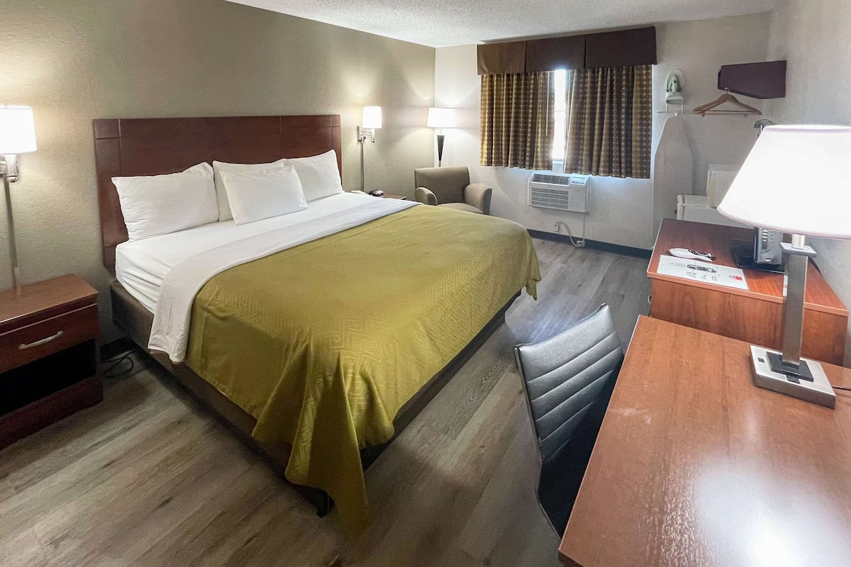 Habitación de hotel con cama, mesitas de noche, un escritorio con lámpara, una silla y una ventana con cortinas.