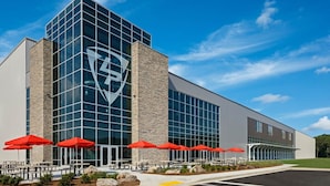 A modern building with a prominent logo on the facade, outdoor seating with red umbrellas, and a clear sky. - Econo Lodge Cartersville-Emerson Lake Point (Cartersville)