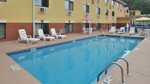 A swimming pool with lounge chairs and umbrellas, surrounded by a building with multiple windows and air conditioning units. - Econo Lodge Cartersville-Emerson Lake Point (Cartersville)