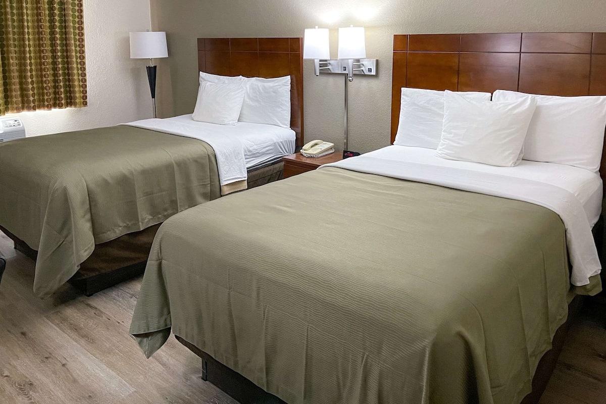Habitación de hotel con dos camas, cada una con cabecero de madera, mesita de noche con lámpara y teléfono.