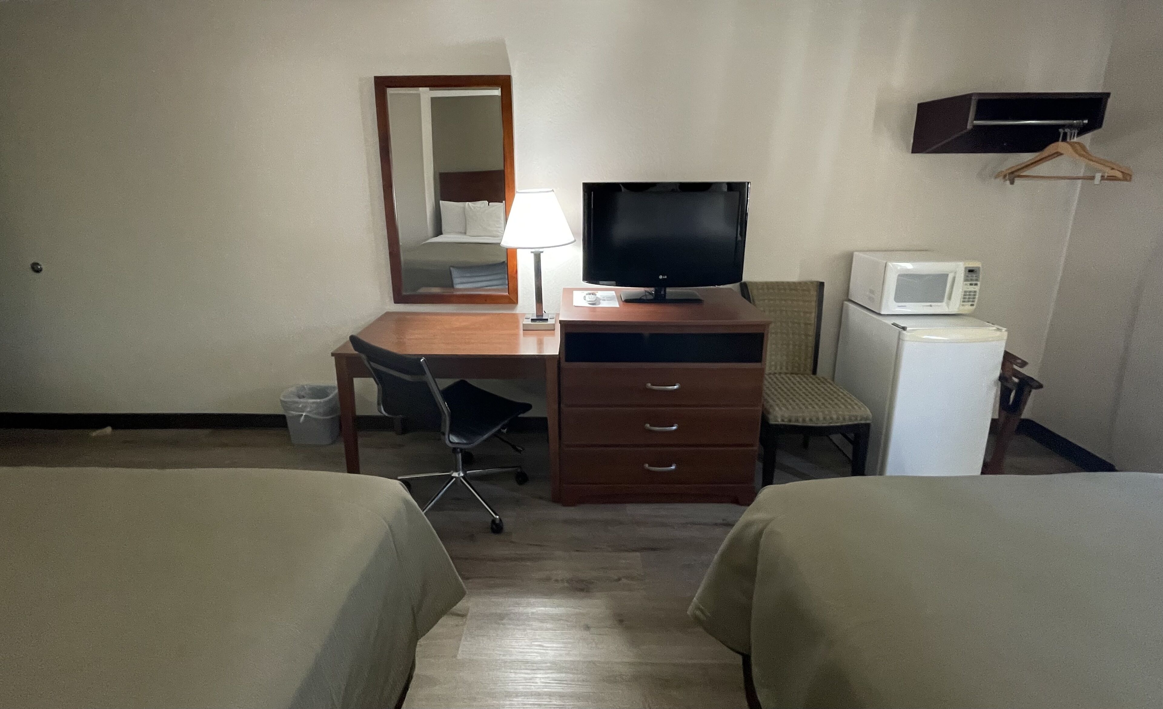 Ein Hotelzimmer mit einem Holztisch, einem Fernseher, einer Mikrowelle und zwei Betten.