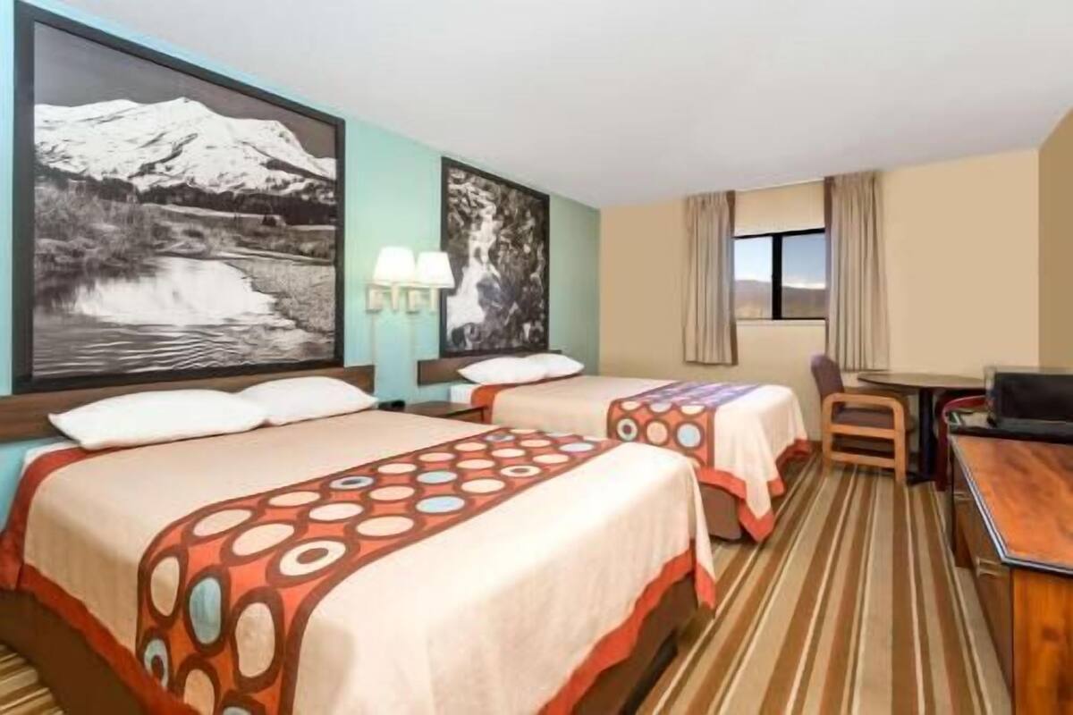 A hotel room with two beds, a desk, a chair, a TV, and two large wall art pieces.
