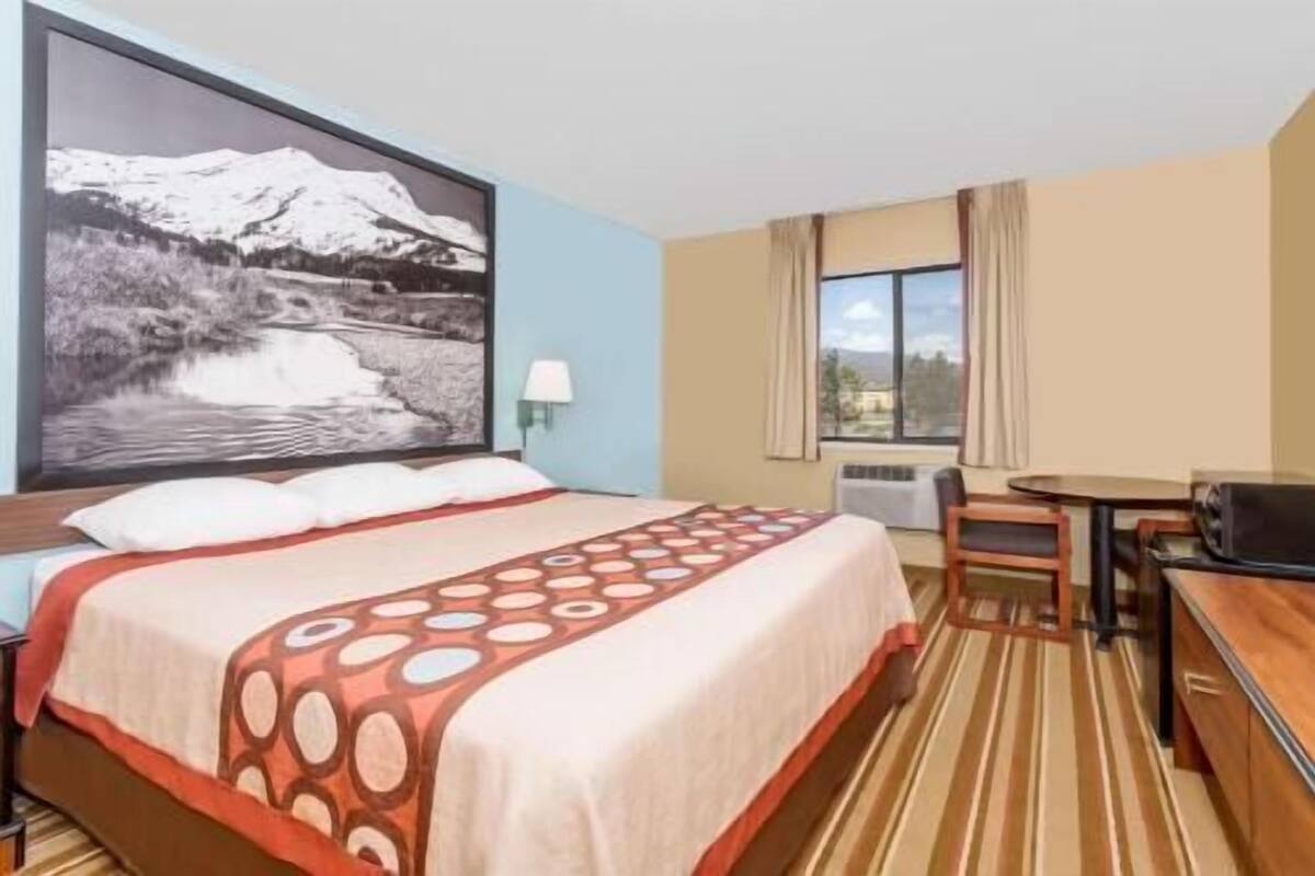 A hotel room with a bed, a desk, a chair, a window with a view, and a wall-mounted lamp.