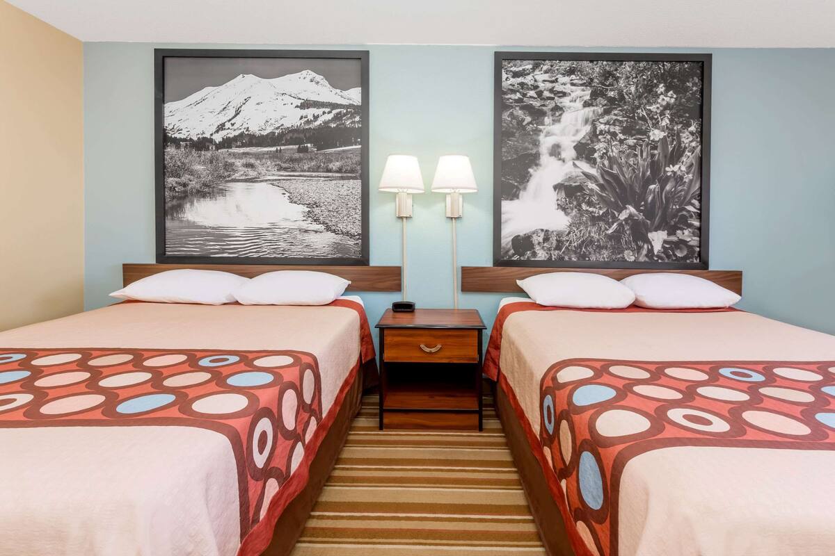 A hotel room with two beds, a nightstand, and two wall-mounted lamps.