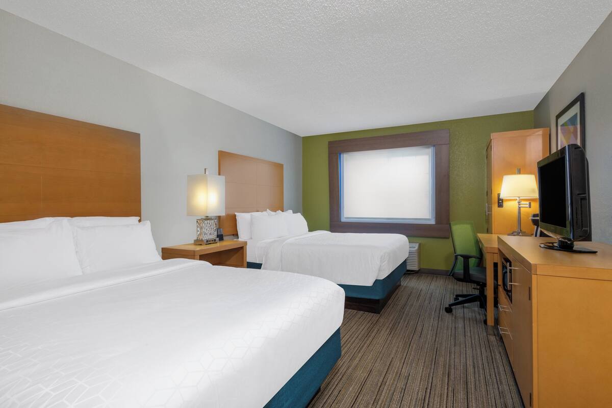A hotel room with two beds, a desk with a TV, a chair, and a window with blinds.