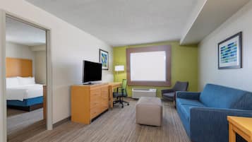 A hotel room with a bed, a desk with a TV, a couch, a chair, and a window.