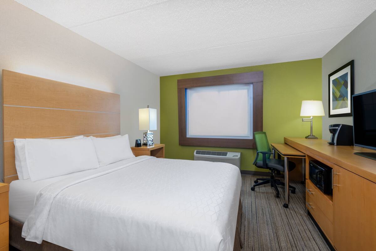 A hotel room with a bed, desk, chair, television, and a window with blinds.