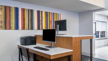 A modern office space with a desk, computer, and printer. A colorful striped artwork is on the wall.