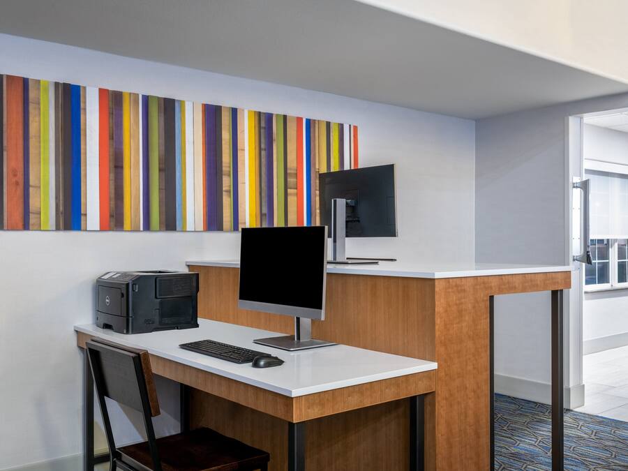 A modern office space with a desk, computer, and printer. A colorful striped artwork is on the wall.