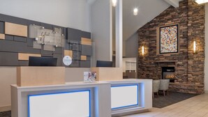 A reception area with a modern design, featuring a stone wall and a fireplace. There are two reception desks with illuminated blue borders.