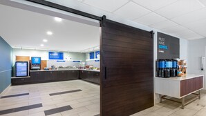 A modern kitchen area with a coffee station, a digital menu board, and a sliding door. - Holiday Inn Express & Suites Wheat Ridge-Denver West by IHG (Wheat Ridge)