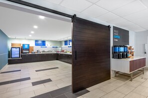 A modern kitchen area with a coffee station, a digital menu board, and a sliding door. - Holiday Inn Express & Suites Wheat Ridge-Denver West by IHG (Wheat Ridge)
