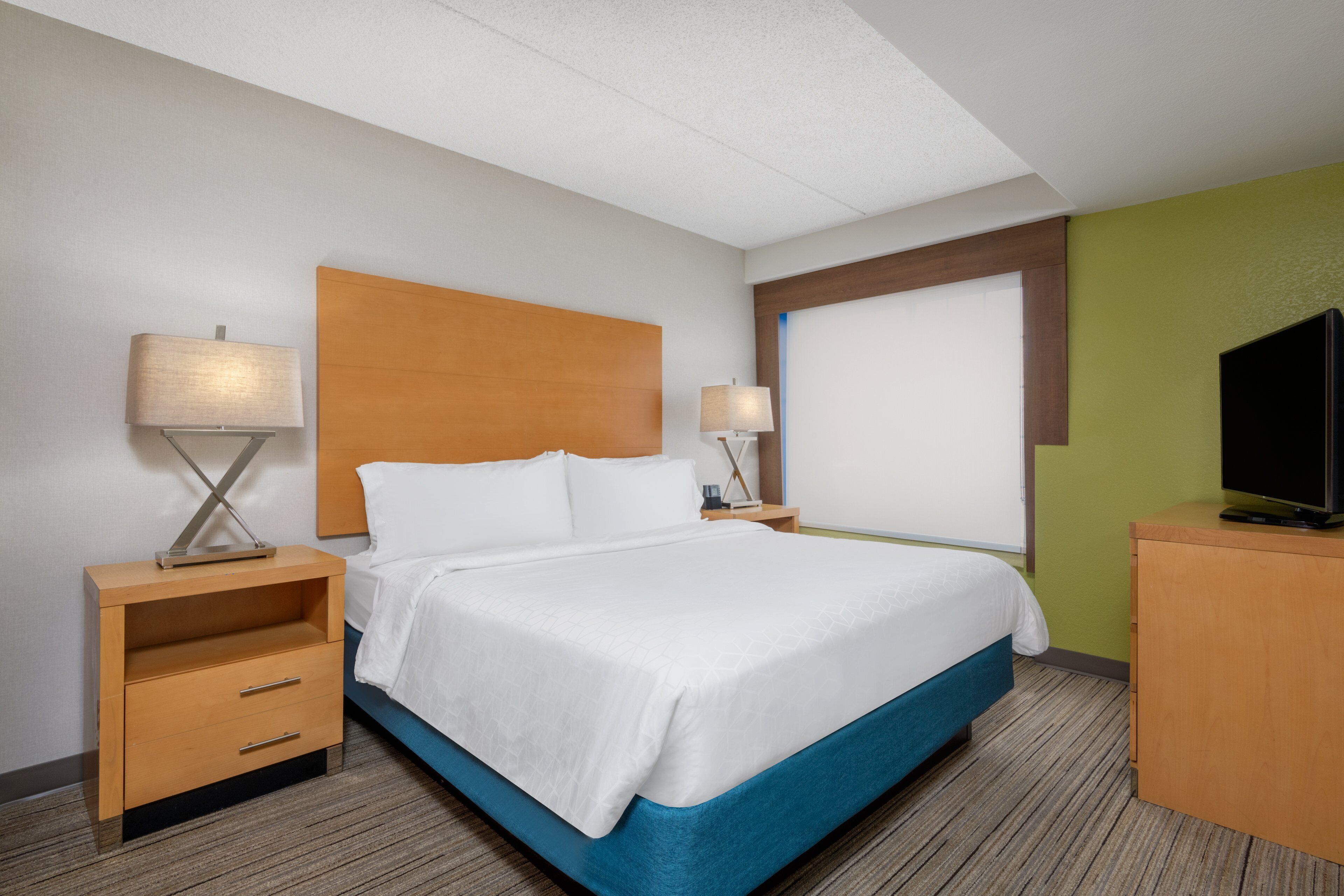 A hotel room with a bed, two bedside tables, a TV, and a window.