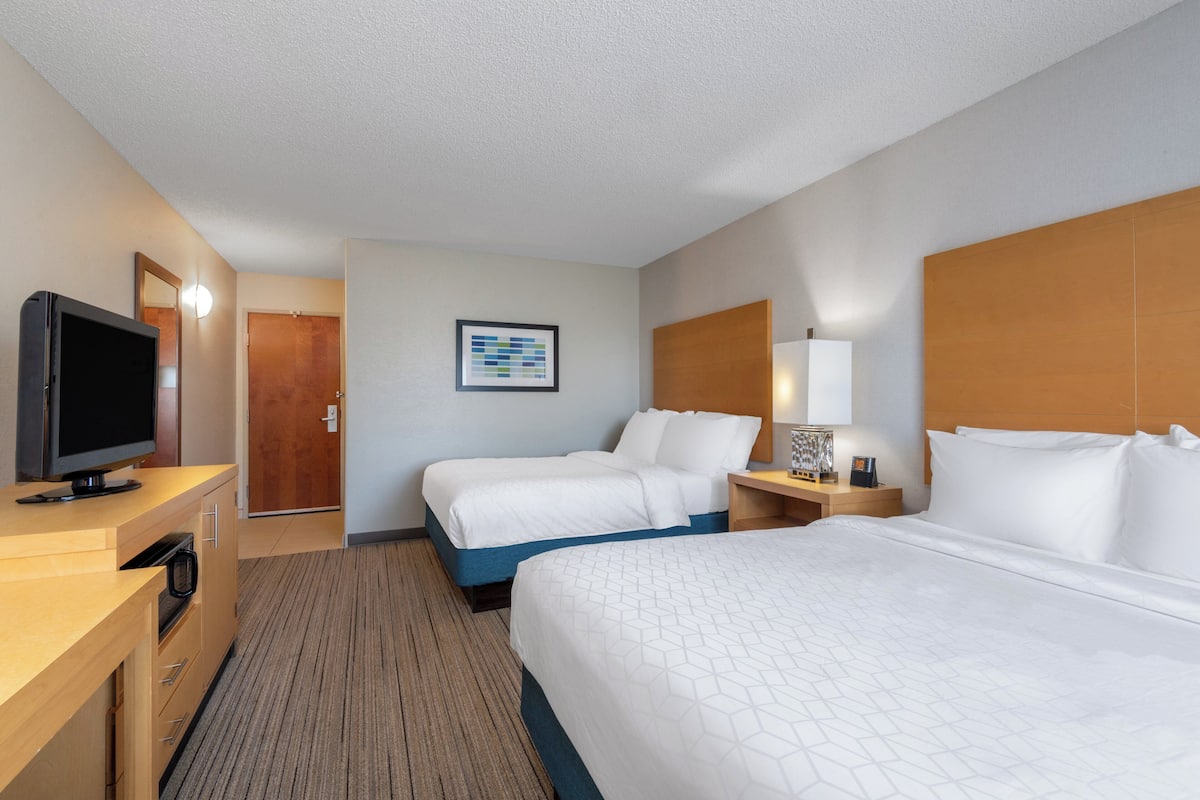 A hotel room with two beds, a TV, a desk, and a framed picture on the wall.