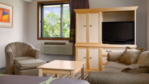Une chambre d’hôtel avec un lit, un canapé, une chaise, une petite table, un téléviseur et une fenêtre avec des rideaux.