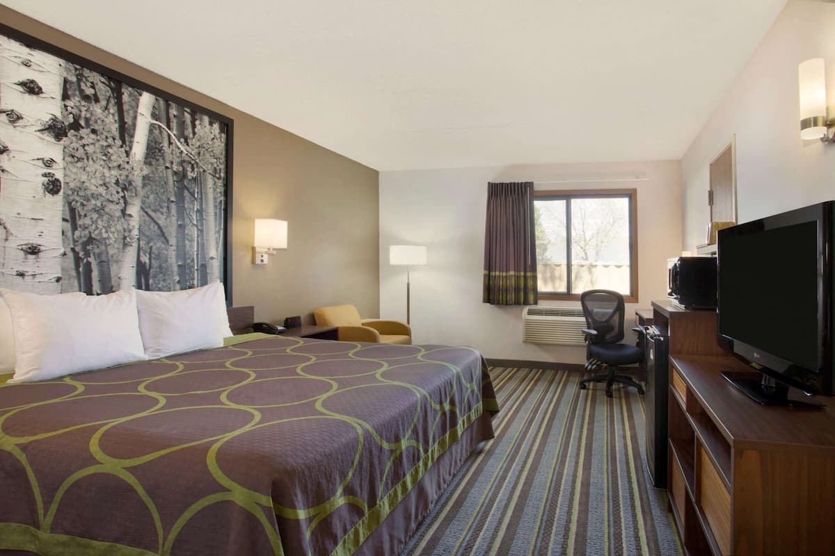 Habitación de hotel con una cama grande, un escritorio con computadora, televisión y ventana con cortinas.