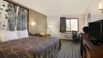 A hotel room with a large bed, a desk with a computer, a television, and a window with curtains.