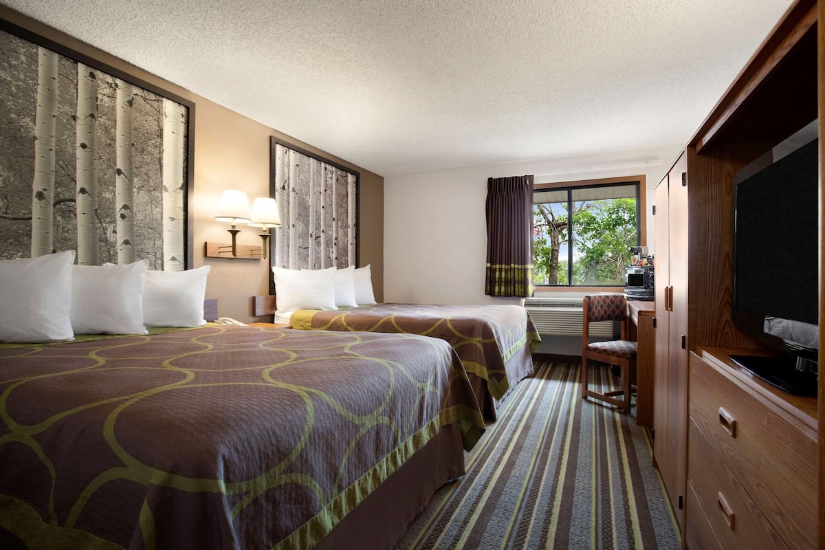 Habitación de hotel con dos camas, televisión, escritorio y ventana con cortinas.
