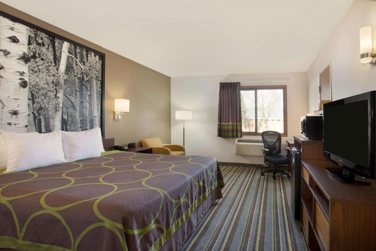 Habitación de hotel con una cama grande, un escritorio con computadora, televisor y ventana con cortinas.