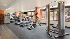 Une salle de sport équipée de tapis de course, de vélos elliptiques et d'une zone d'entraînement avec des poids.