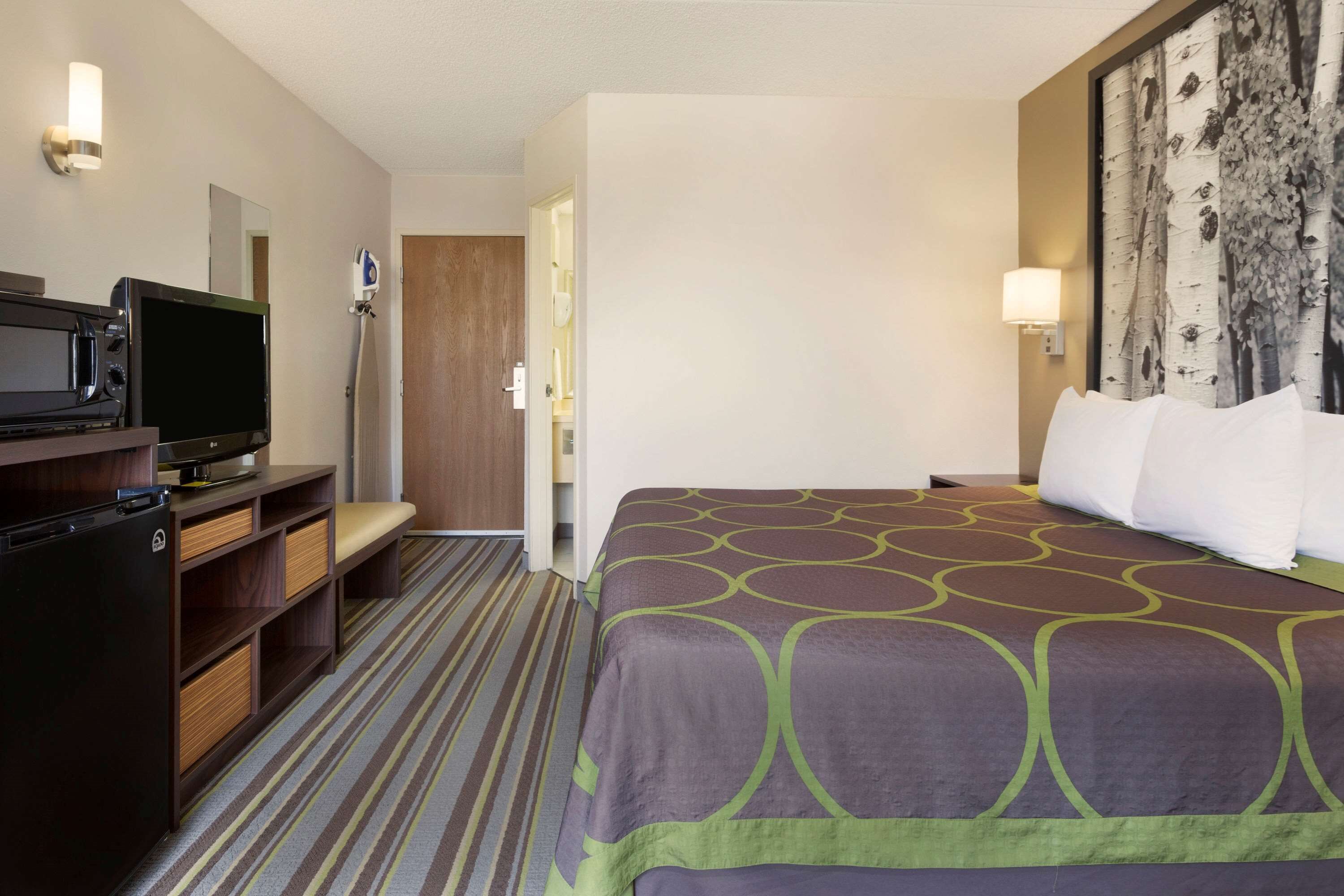 A hotel room with a bed, a TV, a mini-fridge, a desk, and a bathroom door.