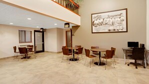 Un grand espace intérieur avec plusieurs tables et chaises, un tableau encadré au mur et un panneau indiquant la sortie.