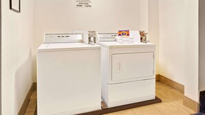 Un espace dédié à la buanderie, équipé de deux machines à laver, d’un distributeur de lessive Tide et d’un panneau indiquant les heures d’utilisation de la buanderie pour les clients.