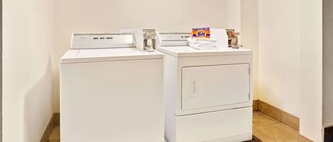 A laundry area with two washing machines, a Tide detergent box, and a sign indicating guest laundry hours.