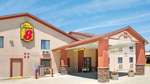 Un hôtel Super 8 avec une façade rouge et beige, une entrée abritée et un ciel bleu dégagé.