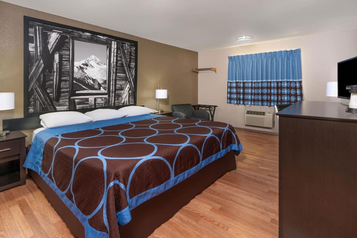 Ein Hotelzimmer mit einem großen Bett, einem Schreibtisch, einem Stuhl, einem Fernseher und einem Bild an der Wand.
