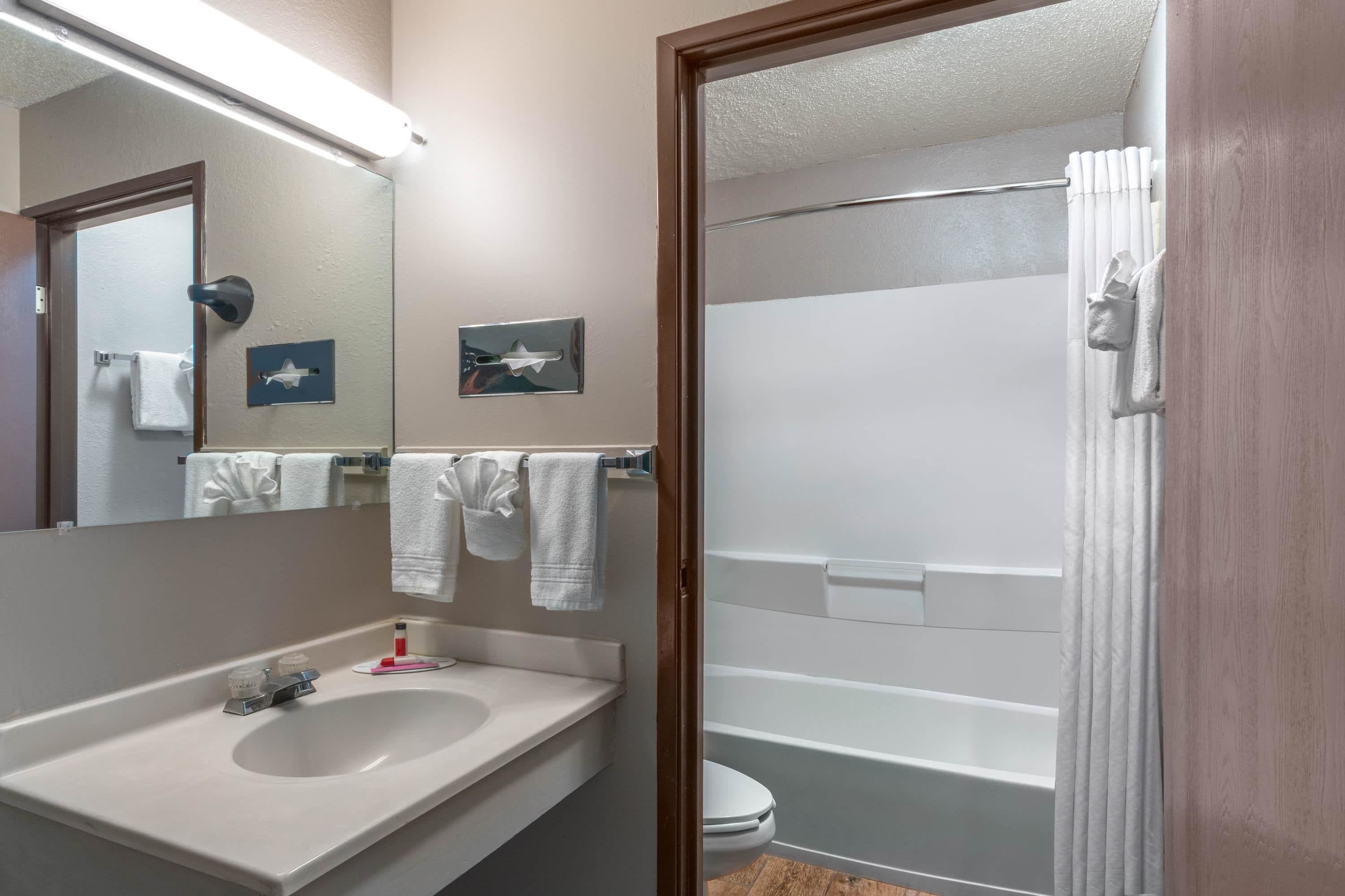 A bathroom with a sink, mirror, towel rack, and a shower area.