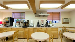 A kitchen with wooden cabinets, a central island with a sink, and a dining area with round tables and chairs.